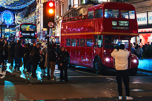A candid street photo of a person taking a picture of a red London bus